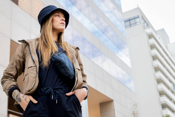 A woman models athleisure wear with a bucket hat and fanny pack against a city backdrop.