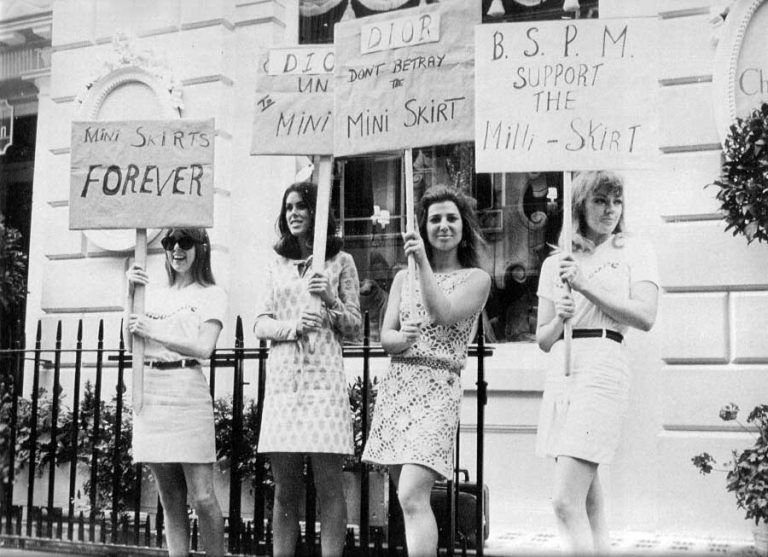 Women holding protest signs in support of mini skirts in front of a building.